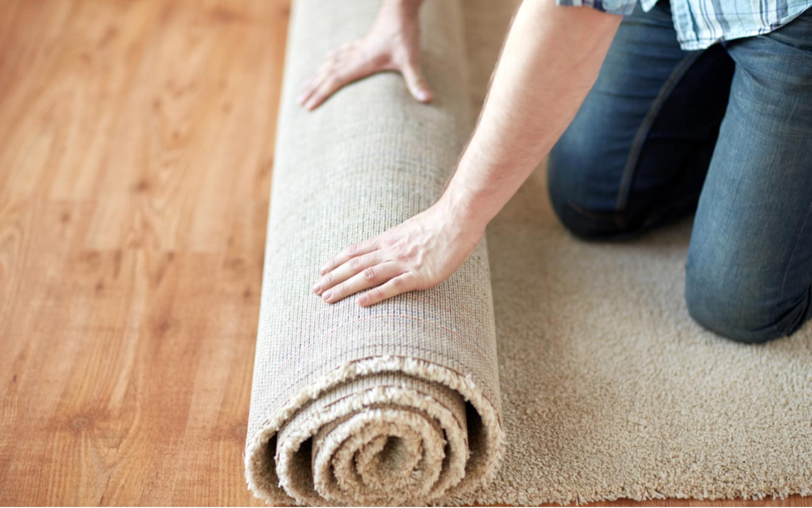 A man unrolling a roll of beige carpet