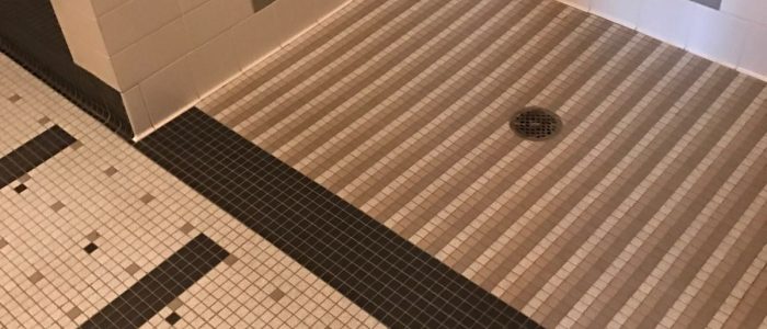 A shower stall with black, grey, and white tiling on the floor and walls
